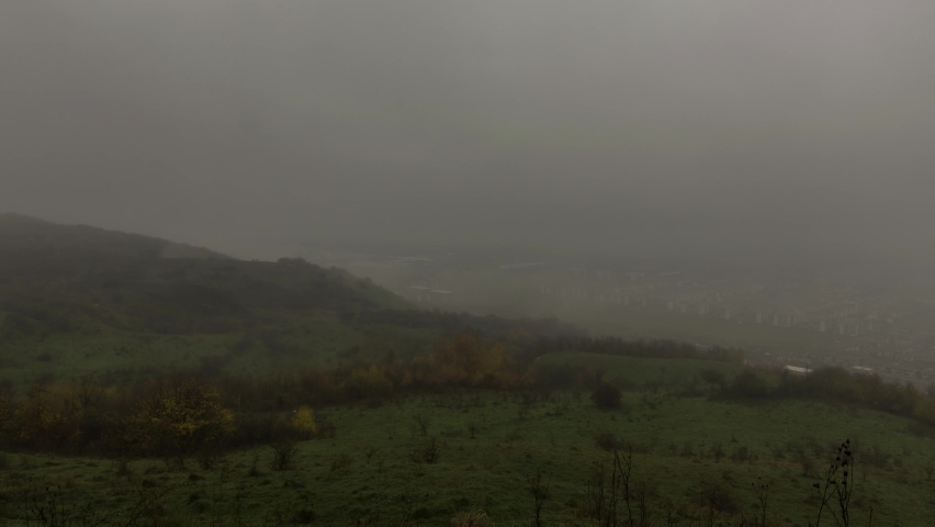 Clouds of fog over spruce forest and small village in the urban area. Autumn day