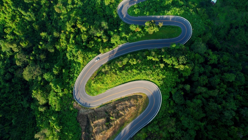 Drone flying above winding road during sunlight, Winding asphalt road through tropical rainforest. amazing zigzag road. countryside landscape. Landmark tourist attractions in Nan Province, Thailand
