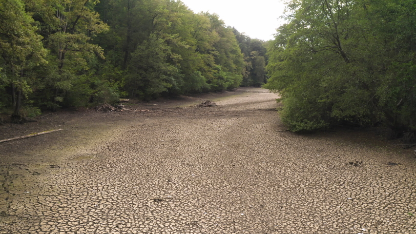 Nature after drought season, reduced river flows, dry river bed between wooded banks, handheld shot.