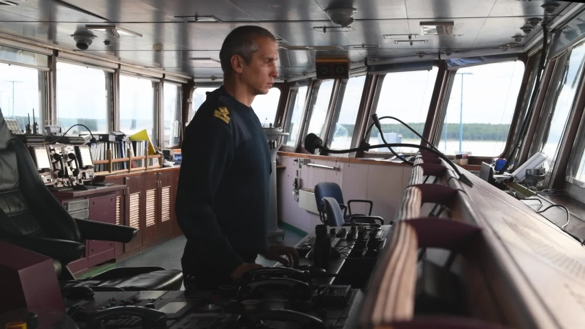 Male deck officer calling traffic control by VHF radio on navigational bridge. Seaman on board of vessel. Commercial shipping. Royalty-Free Stock Footage #1096617927