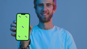 Modern mobile apps. Smiling young guy showing smartphone with mockup green screen, advertising new app, walking