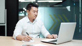 Focused businessman study online watching webinar. Asian business man employee studies video training courses in the office remotely. virtual chat meeting with remote teacher or coach using computer