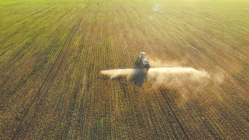Drone footage tractor spreading artificial fertilizers in green field. Farming tractor spraying on field with herbicides. Industrial machine fertilizing a field.Chemicals used by agricultural tractor. Royalty-Free Stock Footage #1096623563