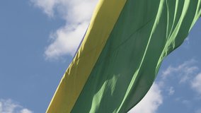 Close up on a Brazilian flag waving on a beautiful sunny day, with the sunlight lighting up the flag. Flag worn by time.