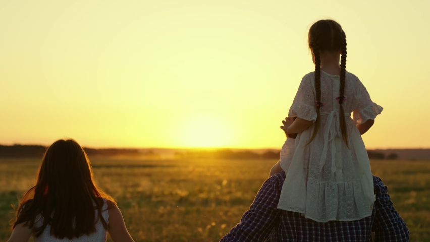 Happy family playing with child at sunset. Kid hugs dad, mother, father run hand in hand across meadow in sun. Aviator Daughter on her fathers shoulders, stretches out her arms, flies like plane