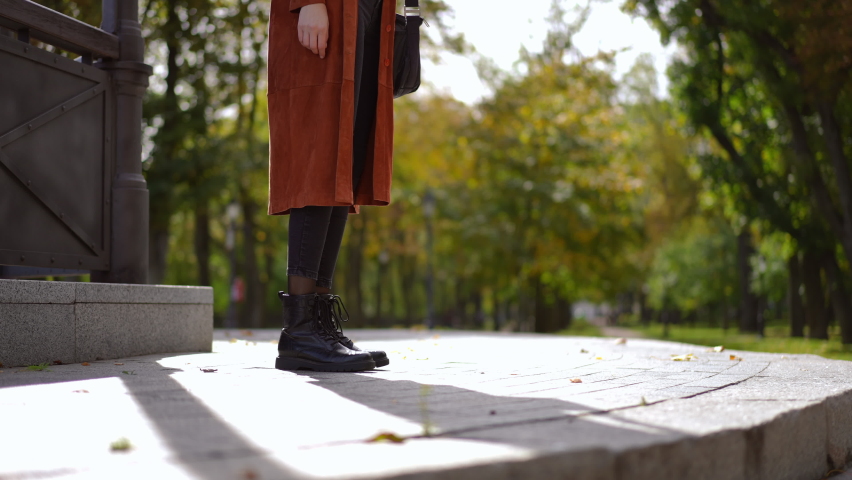 Side view tracking shot of unrecognizable slim stylish young woman walking down on stone stairs in park leaving in slow motion. Confident Caucasian lady strolling outdoors in sunshine