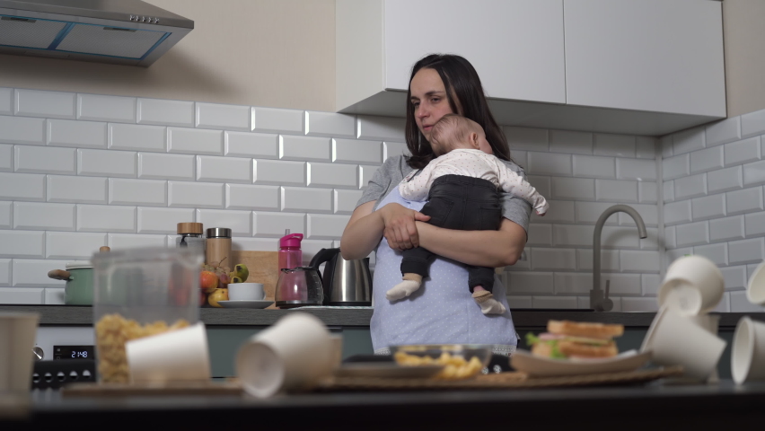 Tired woman lulling the child and trying to drink coffee in messy kitchen. Single mother and baby caring concept | Shutterstock HD Video #1096633199