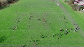 Aerial drone video footage of extensive playing fields situated on the summit of a hill. Showing football players, training, football soccer fields, nets, and strong sunlight