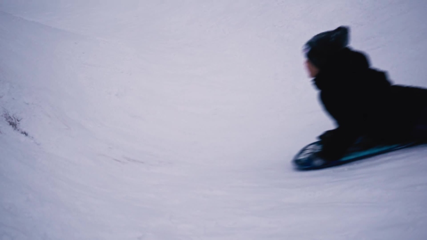 The boy rolls down the snowy slope on an ice rink, a sled. Winter fun Royalty-Free Stock Footage #1096635877