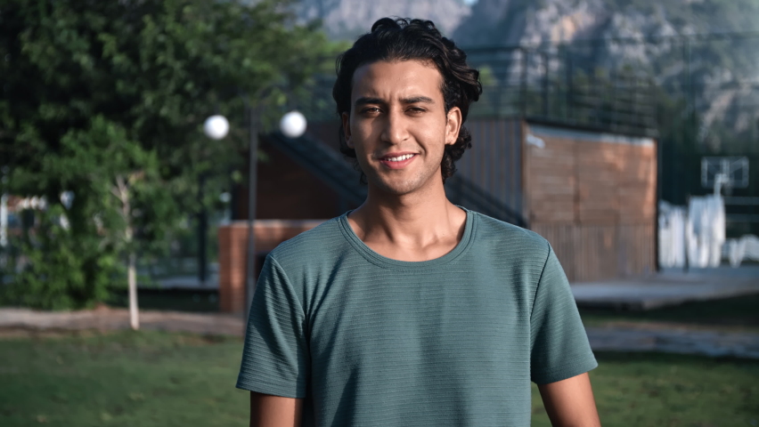 Portrait happy Latino young guy with curly hairs smiling posing summer mountain park landscape. Handsome positive Turkish man relaxing outdoor natural urban garden cliff rock sky green plant scenery  | Shutterstock HD Video #1096637465