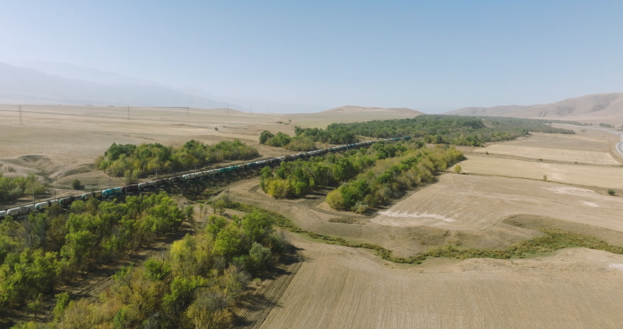 Freight long train carries with oil tank and petrol carriages an locomotive by arid hilly landscape. Railways in savannah . Aerial drone perspective view at summer sunset Royalty-Free Stock Footage #1096640503