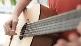 Close-up of a boy playing the guitar while sitting on the couch at home. High quality 4k video. 