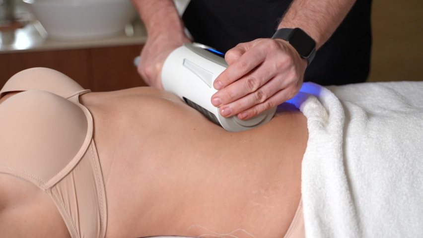 Clinician performs electronic body contouring on stomach of woman