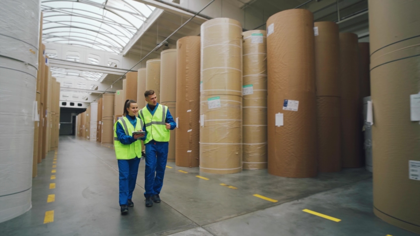 Paper packaging factory. Workers walk through the warehouse among rolls of paper