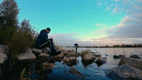 Man photographer with camera on gimbal shooting time lapse clouds in sky with reflection on river shore with stones in water. Beautiful fairy landscape in fast motion