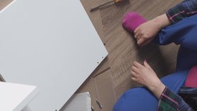 Vertical video. Woman assembling furniture on the floor at home, screwing screw into hole board