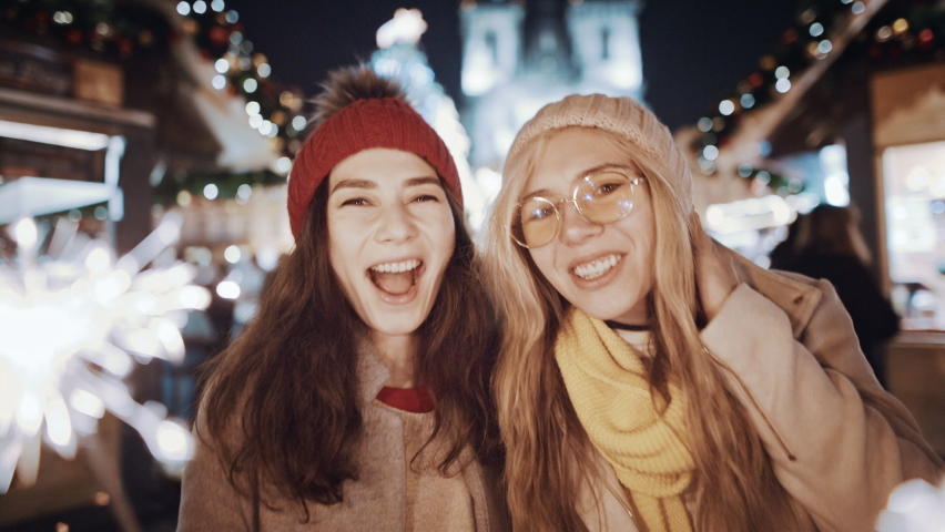 Celebrating New Year Christmas holidays vacation. Happy female friends with sparklers smile at decorated town square. Xmas Christmas winter atmosphere. Excited girls people holding lights in waving | Shutterstock HD Video #1096661853