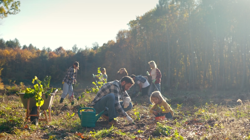 Caucasian father and daughter planting tree together in garden or park. Handome man with small cute child plant seedling of trees. Outside. Family working together in garden. Gardening.