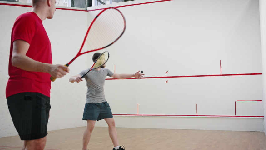 Young men in good physical shapes play squash. Athletes follow movement of ball carefully and move actively hitting rubber ball against front wall closeup Royalty-Free Stock Footage #1096663869