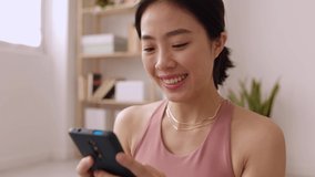 Young asian woman using mobile phone after workout exercise routine. Chinese fitness female relaxing with cellphone while exercising at home - High quality 4k footage