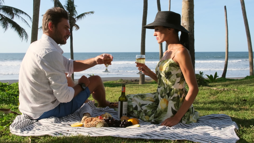 a girl and a guy on the ocean celebrating a honeymoon trip to Bali, a Romantic picnic. Concept of a summer picnic outdoors with blanket, man feeding woman, cheese and wine. Royalty-Free Stock Footage #1096667505