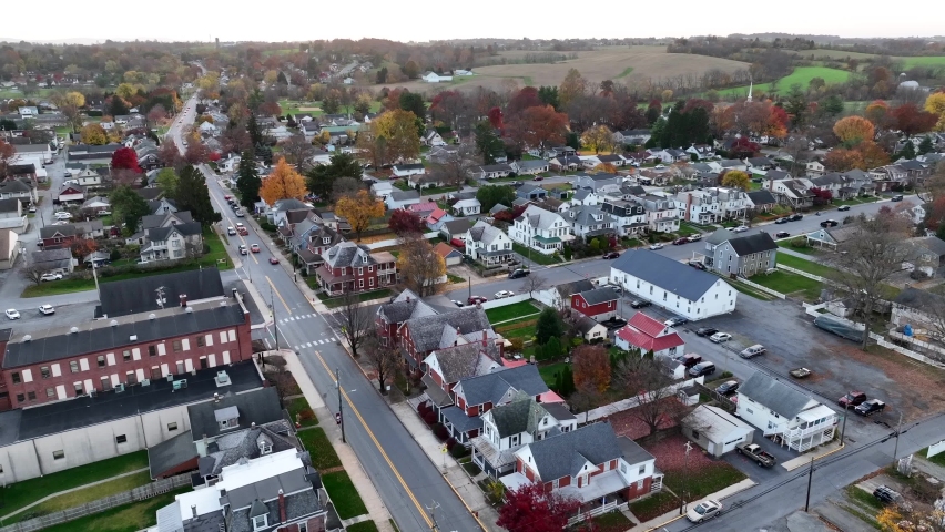 Cars and trucks drive through small town in USA. Rising aerial reveals rural countryside and downtown city.