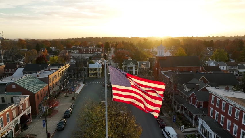 Warm glow of autumn sunset reflects on USA flag waving in breeze. Aerial view. Proud to be an American theme.