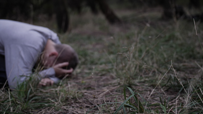 The feet of Jesus Christ walking up to a sad young man laying on the ground crying with his head in his hands.