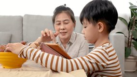 Mother teaching handsome kid to review lessons by tablet during the holidays, woman and son sit on warm floor and learn lesson together in living room. domestic life and family leisure time concept.