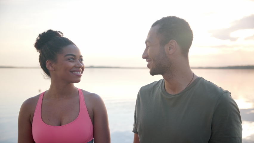 Close up portrait of happy smiling beautiful woman and handsome man looking at camera standing outside on nature with lake on background. Cheerful couple of athletes outdoor on lake on dock