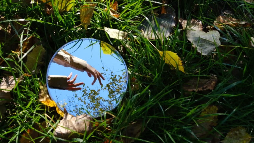 The reflections of woman hands moving in round mirror lying in nature environment with autumn atmosphere with fooliage and green grass in sunny day Royalty-Free Stock Footage #1096683681