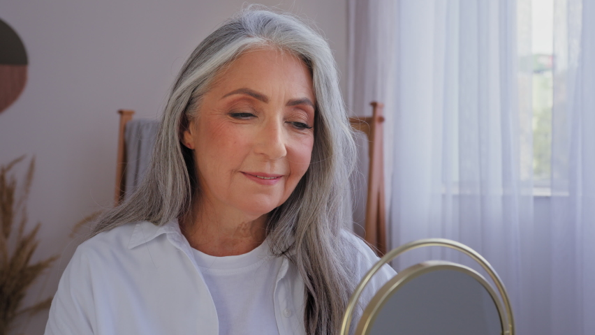 Caucasian 60s aged senior mature lady old gray-haired 50s woman female with mirror smile looking at camera beautiful aging wrinkled face anti-aging surgery lifting skin care moisturizing rejuvenation Royalty-Free Stock Footage #1096684541