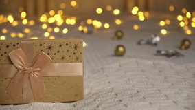 Gold Colored Gift Box on Blurred Abstract Warm Living Room Decor. New Year Video Banner with Copy Space for Text. Christmas Lights. Holiday Backdrop for Display of Advertise Product. Shopping, Sale 