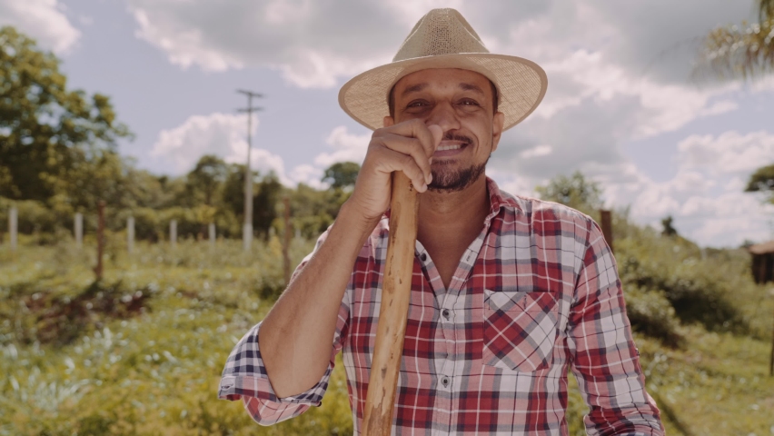 Portrait of young man in the casual shirt holding his hoe in the farm. Farm tool. Latin man. Premium Cinematic 4K Royalty-Free Stock Footage #1096687045
