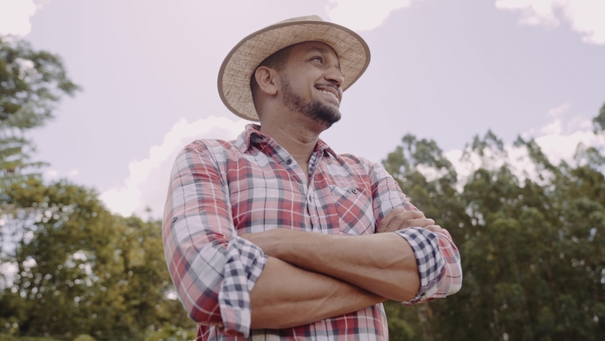 Portrait of young farmer man with crossing hands in the casual shirt and hat in the farm. Premium Cinematic 4K