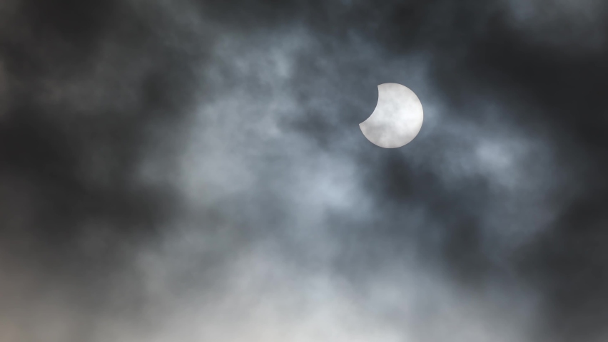 Partial solar eclipse with dark clouds passing in the foreground. Royalty-Free Stock Footage #1096689741