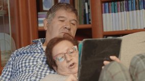 Happy spanish mature couple sitting on a sofa while looking at a tablet at home