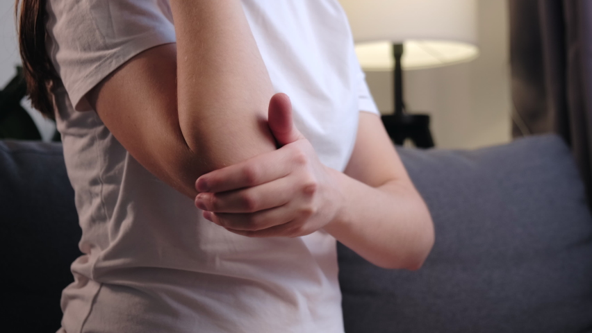 Close up of unhealthy young caucasian woman touches elbow in morning and massages sitting on grey couch at home, warming up injured hand after trauma. Arthritis of joints pain in elbow concept Royalty-Free Stock Footage #1096699881