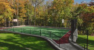 Aerial video of a new green and red outdoor basketball court at school playground or part.  Court includes retaining walls and black vinyl coated chain link fence.	