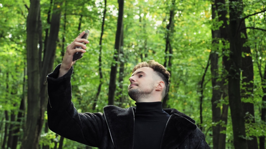 Lost man in forest holding a mobile phone not receiving any cellphone signal. Upset man holding smartphone up high, trying to catch cellular network in autumn wood. No connection, battery problem. Royalty-Free Stock Footage #1096713201