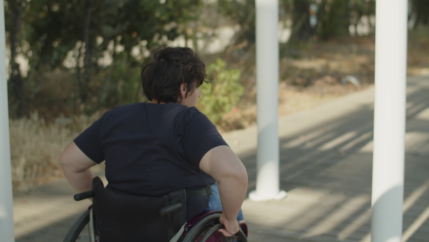 Young woman with disability wheeling in park. Caucasian woman using wheelchair and walking outdoors. Woman with disability concept