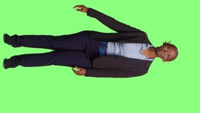 Vertical video: African american businesswoman doing green screen advertisement over full body greenscreen backdrop. Female manager showing ad example and promotion on studio background, smiling adult