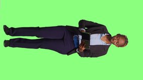 Vertical video: Confident manager using digital tablet on greenscreen backdrop, full body green screen. Browsing internet on portable device with touchscreen, working with wireless modern gadget.