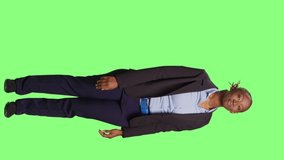 Vertical video: African american office worker doing greenscreen advertisement over full body backdrop. Businesswoman manager showing ad example and promotion on studio green screen, smiling girl.