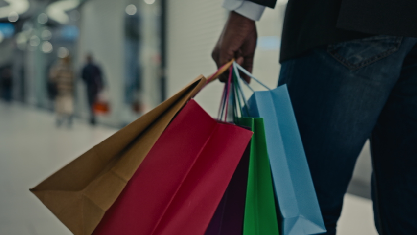 Unrecognizable African unknown man customer buyer businessman male legs with shopping bags gifts purchases walking in mall indoors in shop store moving walk consumer after buying Black Friday discount Royalty-Free Stock Footage #1096722045