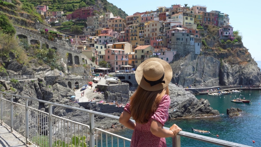 Young tourist woman enjoying traveling in Italy. Beautiful stylish girl with hat and dress looking at Manarola village overhanging the sea, Cinque Terre, Italy. Royalty-Free Stock Footage #1096727179