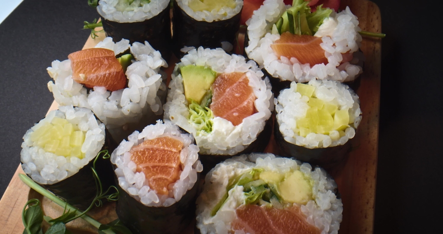 Picking up with chopsticks a delicious sushi from a wooden plate. Variety of types sushi with salmon fish, avocado, fish, cucumber Set of delicious Japanese sushi rolls. Eating sushi in a restaurant. | Shutterstock HD Video #1096730127
