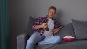A young man drinking beer while sitting on the couch. Concept of free time, sport and entertainment. 