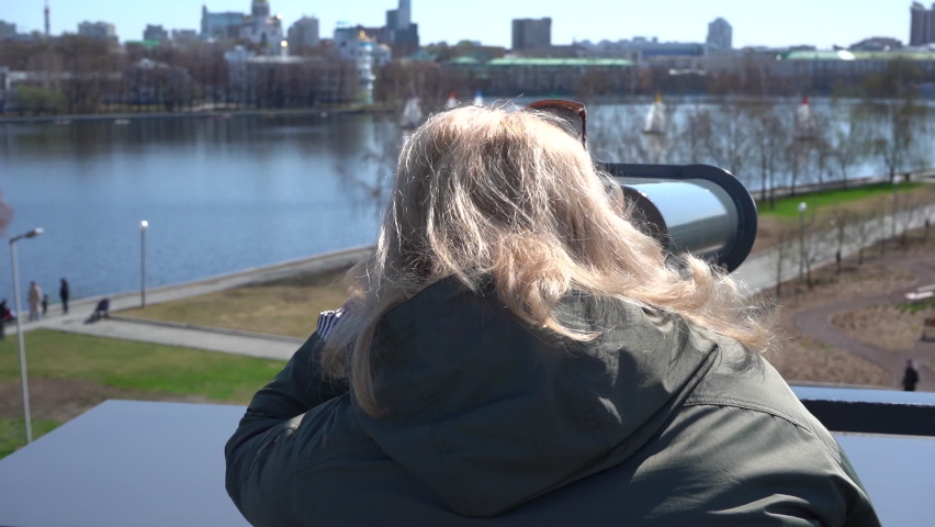 Rear view of a woman looking through binoculars with a coin, standing at the observation point. High quality FullHD footage