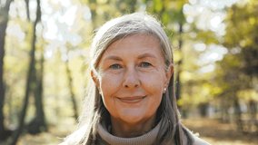 Close-up portrait of naturally beautiful senior cute gray-haired woman standing in park in autumn wearing coat looking at camera smiling. Pretty mature kind good-looking female on fresh air. - Powered by Shutterstock - Get 15% off with code: PIKWIZARD15